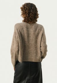 Beige gebreide trui met een relaxed fit, geribbelde zoom en iets overgrote mouwen, gecombineerd met een zwarte leren rok.