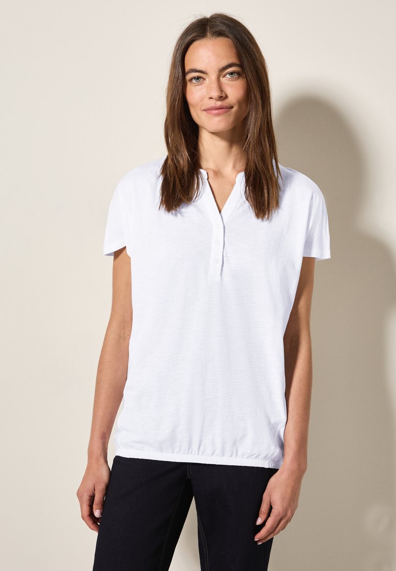 Witte polo shirt met korte mouwen, voorzien van een knoopsluiting en elastische zoom. Gemaakt van zachte stof, met een ontspannen pasvorm en een gestructureerde afwerking.