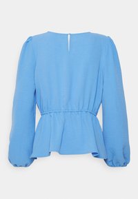 Světle modrý top s kulatým výstřihem, nařasenými rukávy a peplum siluetou. Má otevření na zadní straně ve tvaru klíče se zapínáním na knoflík.
