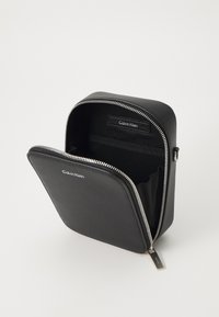 Sort lærreimmet toalettmappe med sølvfarge detaljer, med et ensfarget design og indre lommer, merket med "Calvin Klein."