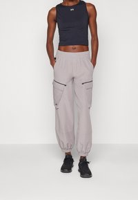 Harmaalta cargo-housut elastisilla hihansuilla, joissa on kaksi sivutaskua ja mustat yksityiskohdat. Vaatteena tiukka musta crop-top ja mustat urheilukengät.