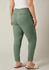 Groene, lichte, textuur broek met een elastische tailleband, aansluitend bij de enkels en twee achterzakken. Gedragen met witte, open sandaaltjes.