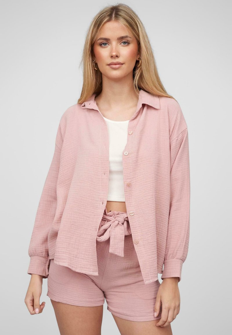 Camicia rosa con texture, colletto a camicia, vestibilità ampia e maniche arrotolate, abbinata a pantaloni shorts dello stesso colore con vita regolabile. 
