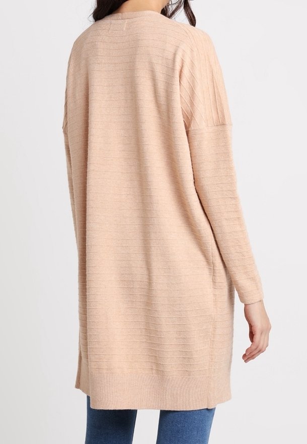 Lång, löst sittande kofta i mjuk persikofärgad stickning med vertikal ribbad textur. Har en rundad halsringning och slitsar i sidorna vid fållen.