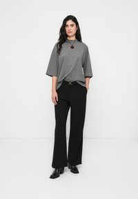 Γκρι υπερμεγέθη μπλουζάκι με κοντά μανίκια, συνδυασμένο με μαύρο παντελόνι ψηλόμεσο. Μαύρα μποτάκια αστραγάλου και ένα κόκκινο κολιέ με μενταγιόν ολοκληρώνουν το σύνολο.