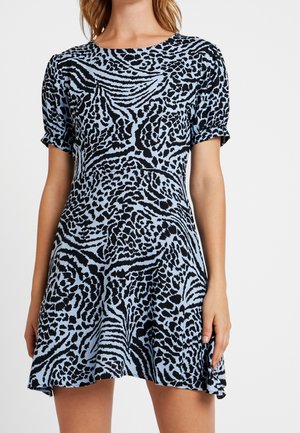 Kvinde iført en kortærmet, blå og sort dyreprintkjole med rund halsudskæring og let udvidet nederdel.