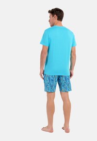 T-shirt turquoise assorti avec un short bleu à motifs featuring des feuilles tropicales en jaune et vert, conçu pour un style décontracté.
