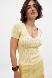 Geltonas megztukas su trumpomis rankovėmis, turintis V formos iškirptę, banguotą tekstūrą ir subtilų atvirą audimą. Lengvas, prigludęs dizainas.