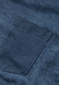 Top in tessuto denim con tasca singola. Colore blu scuro con una leggera texture. La tasca ha bordi puliti e cuciture coordinate.