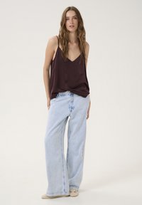 Camicetta in satin bordeaux con spalline sottili abbinata a jeans a gamba larga di colore blu chiaro. L'outfit presenta una vestibilità rilassata e dettagli di lavaggio sottili.