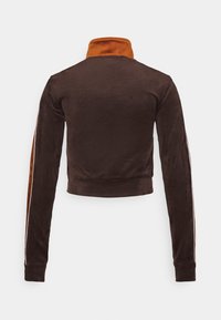 Veste cropped en velours marron avec un col haut orange et des rayures orange et blanches sur les manches, vue de dos.