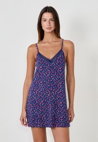 Robe nuisette marine avec imprimé floral rouge et blanc. Elle dispose de bretelles fines et d'une bordure en dentelle au niveau du décolleté. Tissu léger et coupe décontractée.