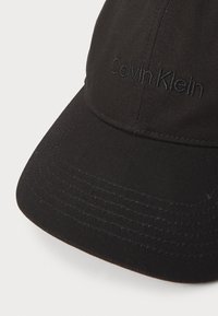 Black baseball cap made of canvas, featuring a structured shape, curved visor, and embroidered "Calvin Klein" logo in the same color.