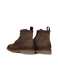 Bruine suède enkelboots met een ronde neus, vetersluiting aan de voorkant, zijrits en een gestructureerd oppervlak. Rubberen zool met een lichte hak.