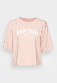 Lyserød cropped t-shirt lavet af blødt stof. Har hvid tekst "NEW YORK" i en bue på forsiden, med opretstående ærmer og en afslappet pasform.
