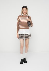 Bruin en wit gestreepte trui, witte shirt eronder, geruite rok, zwarte schoenen, witte sokken. Eenvoudig ontwerp met gelaagde texturen.