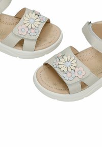 Sandales pour enfants beige avec semelles blanches, décorées d'appliqués floraux roses, crème et gris sur les brides.