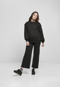 Felpa nera con maniche lunghe, design semplice e polsini a coste, abbinata a pantaloni neri a gamba larga e sneakers nere con suola in gomma.