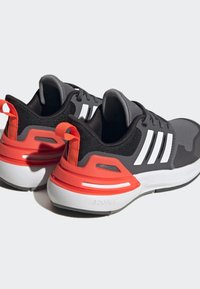 Zapatillas deportivas en negro y gris con un acento blanco, que cuentan con un upper texturizado, un contrafuerte en naranja y una suela blanca acolchada.
