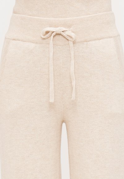 Beige knit sweatpants with a ribbed waistband, featuring a drawstring, side pockets, and a soft texture.