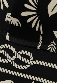 Zwarte stof met een wit botanisch en touwpatroon, met een gladde textuur en contrasterende stiksel langs de rand.