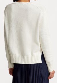 Suéter blanco de punto con dobladillo y puños acanalados. Presenta un ajuste holgado y un escote redondo, con un patrón texturizado en toda la prenda.