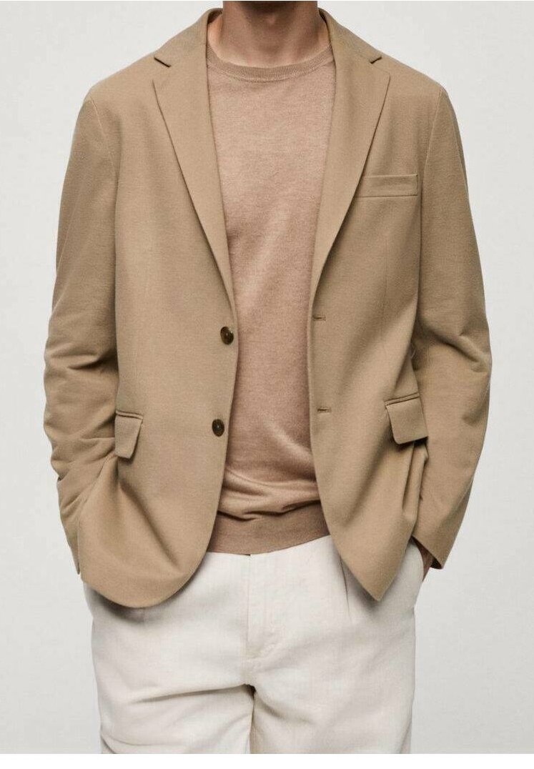 Blazer beige avec deux poches avant et boutons marron, associé à un pull beige clair. Un pantalon blanc complète la tenue. Texture lisse tout au long.