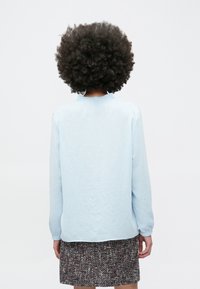 Helehall sinine, pika varrukaga triiksärk tekstuurse viimistlusega ja kraega, kombineeritud mustrilise tweed-seelikuga. Tagantvaade.