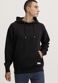 Sudadera negra con capucha, hecha de una tela suave. Presenta un bolsillo tipo canguro, cordones ajustables y puños acanalados en el dobladillo.