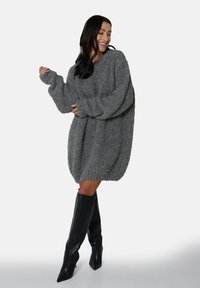 Szary, oversize sweter w formie sukienki, wykonany z miękkiej, teksturowanej tkaniny, z długimi rękawami i ściąganym dołem, zestawiony z czarnymi kozakami za kolano.