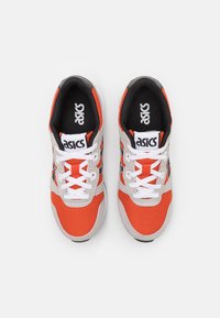Sneaker arancione e grigio con tomaia in rete, colletto imbottito, lacci bianchi e bordatura nera. Presenta il logo Asics sulla linguetta e sul lato.