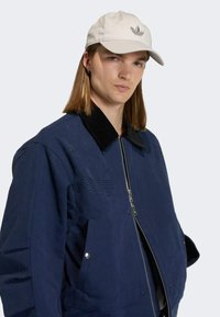 Námořnická modrá bomber bunda s černým kordovým límcem, zipovým uzávěrem a vyšitým logem. Doplněná světlobéžovou kšiltovkou.