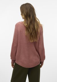Un pull en tricot rose surdimensionné avec un tissage texturé, des poignets et un ourlet côtelés, associé à un pantalon vert foncé, vu de dos.