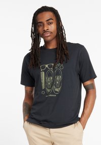 Camiseta negra con un diseño gráfico de zapatillas, gafas de sol y un peine en verde. Material de algodón, con mangas cortas y cuello redondo.