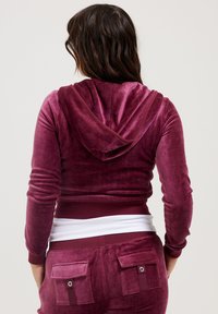 Velvet hooded jacket in deep mauve, fitted design, with a white ribbed band at the waist and pocket accents on the back.