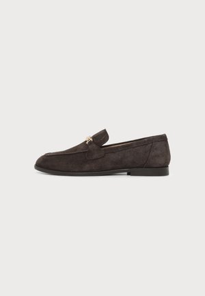 Mocassin en daim marron foncé avec un petit détail métallique doré sur le dessus, semelle plate noire et bout arrondi, vu de côté.