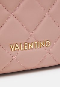 Quilted pink leather handbag featuring gold "VALENTINO" logo. Smooth texture with decorative stitching and geometric pattern.