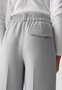 Light gray high-waisted trousers with a textured fabric, elastic waistband, and a single back pocket detail.