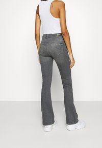 Höga, utsvängda mörkgrå jeans med bakfickor, subtila blekningar och en slät textur, kombinerat med en vit tanktopp och vita sneakers.