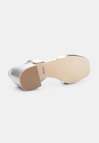 Silver high-heeled shoe with a rounded toe and open back. Features a textured rubber sole and a smooth metallic finish on the upper.