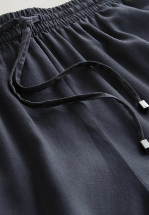 Tmavomodré šortky s elastickým pásom vyrobené z mäkkej látky, sťahované šnúrkou s kovovými koncovkami a jemnými záhybmi na materiáli.