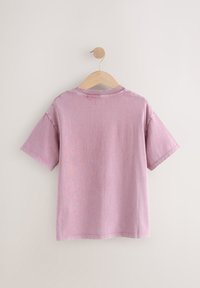 Rövid ujjú, rózsaszín pamut póló hátulról, fa vállfán, kerek nyakkivágással és varrott szegéllyel.