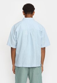 Camicia a maniche corte a righe blu e bianche con colletto classico, piega sul retro e vestibilità morbida. Tessuto leggero con finitura testurizzata.