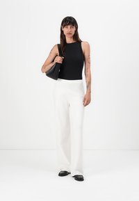 Zwarte geribbelde mouwloze top, witte broek met wijde pijpen en zwarte tas. Gladde textuur, hoge taille, relaxed fit, minimalistisch ontwerp.