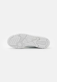 Bílá sportovní podrážka s texturovanou gumou, která má hroty pro trakci a branding "new balance". Hladké a mírně zvýšené vzory.