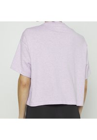 Liliowy crop top z krótkim rękawem wykonany z lekkiej mieszanki bawełny. Posiada okrągły dekolt oraz luźny krój z opadającymi ramionami.