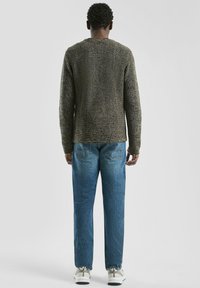 Gebreide trui in donker groen-bruin, met een gewatteerd patroon, ronde halslijn, gecombineerd met lichtblauwe rechte jeans en witte sneakers.