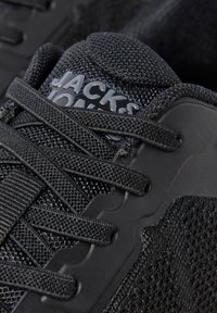 Крупен план на черен маратон Jack & Jones, показващ мрежеста тъкан, текстурирани връзки и лого на подплатения език.