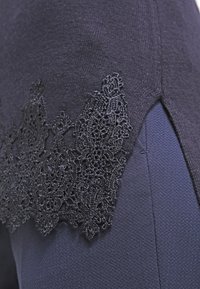 Mörkblå tröja av texturerad stickad tyg med svart spetsdetalj längs sidorna, vilket ger intrikata mönster och kontrast.