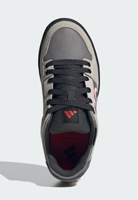 Gray athletic shoe with a mesh upper, black laces, and a red logo accent. Features a padded collar and textured rubber sole.